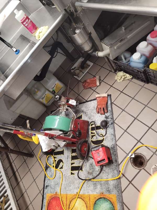 Equipo mecánico de limpieza junto a un drenaje de piso abierto en la cocina comercial.